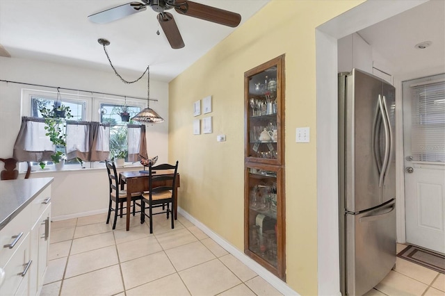 kitchen with light tile patterned floors, baseboards, freestanding refrigerator, ceiling fan, and white cabinetry