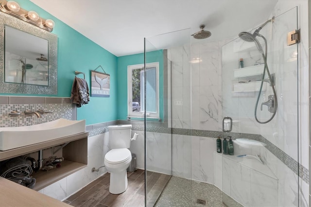 bathroom featuring a marble finish shower, wood finish floors, a sink, tile walls, and toilet