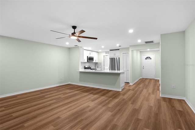 kitchen with visible vents, wood finished floors, white cabinetry, stainless steel appliances, and a peninsula