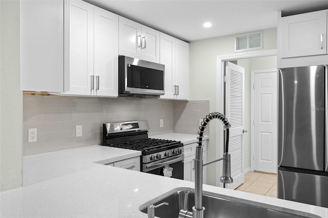 kitchen featuring light tile patterned floors, visible vents, stainless steel appliances, white cabinetry, and backsplash