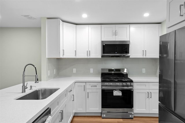 kitchen with light wood-style flooring, appliances with stainless steel finishes, white cabinetry, and a sink