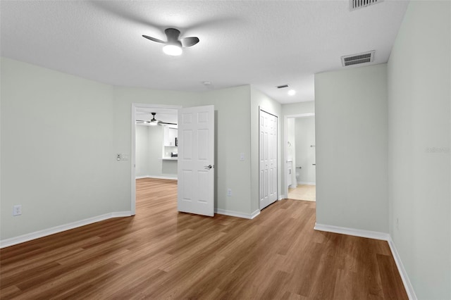 empty room featuring a ceiling fan, wood finished floors, visible vents, baseboards, and a textured ceiling