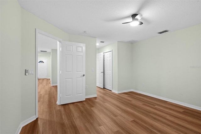 unfurnished bedroom featuring wood finished floors, visible vents, baseboards, ceiling fan, and a closet