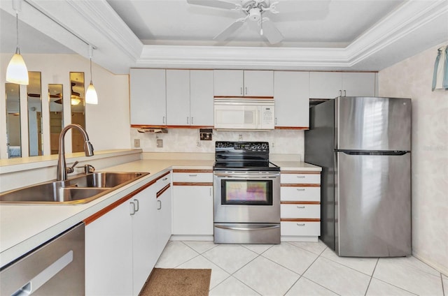 kitchen featuring light tile patterned floors, a tray ceiling, ornamental molding, a sink, and appliances with stainless steel finishes