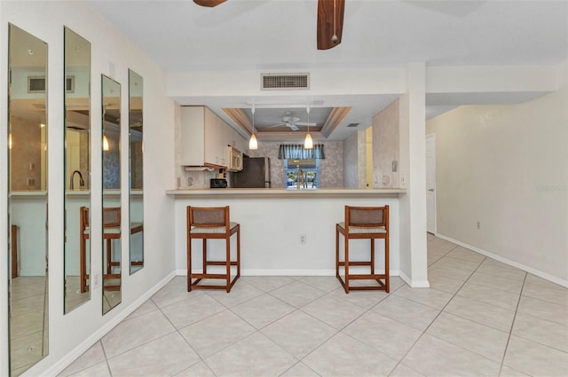 kitchen with visible vents, freestanding refrigerator, white microwave, a raised ceiling, and a ceiling fan