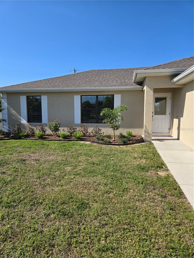 view of front of home with stucco siding, a front yard, and roof with shingles