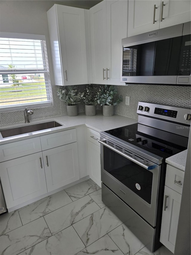 kitchen featuring a sink, decorative backsplash, stainless steel appliances, white cabinets, and marble finish floor