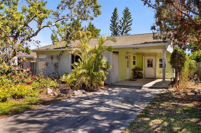 view of front of house with a carport, roof with shingles, and driveway