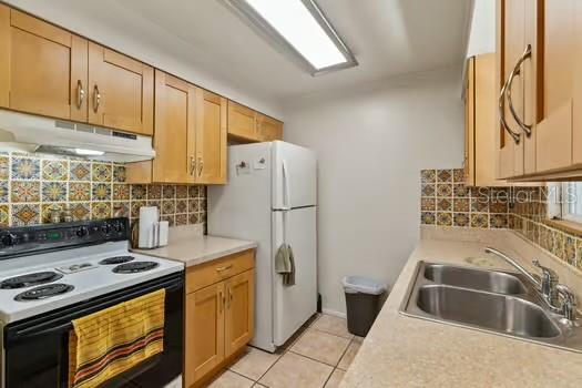 kitchen featuring under cabinet range hood, light countertops, range with electric stovetop, freestanding refrigerator, and a sink