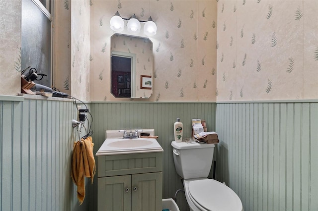 bathroom with a wainscoted wall, toilet, wallpapered walls, and vanity