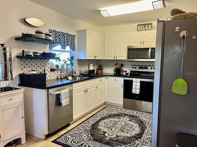 kitchen featuring light tile patterned flooring, a sink, appliances with stainless steel finishes, white cabinetry, and tasteful backsplash