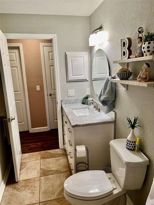 bathroom with vanity, baseboards, tile patterned floors, toilet, and a textured wall