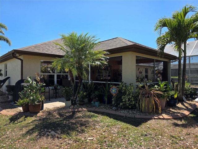 back of property featuring stucco siding, roof with shingles, and a sunroom