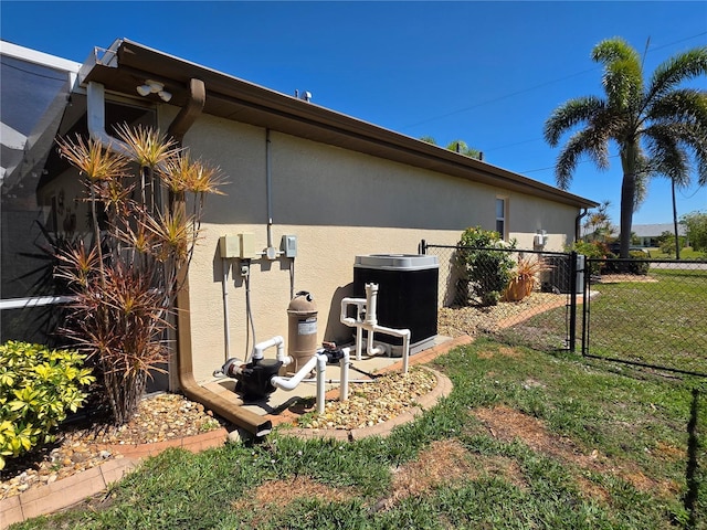 view of side of home with stucco siding, a lawn, central AC, and fence