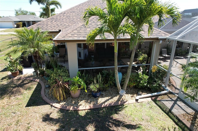 rear view of property with stucco siding, a patio, a lanai, and a shingled roof