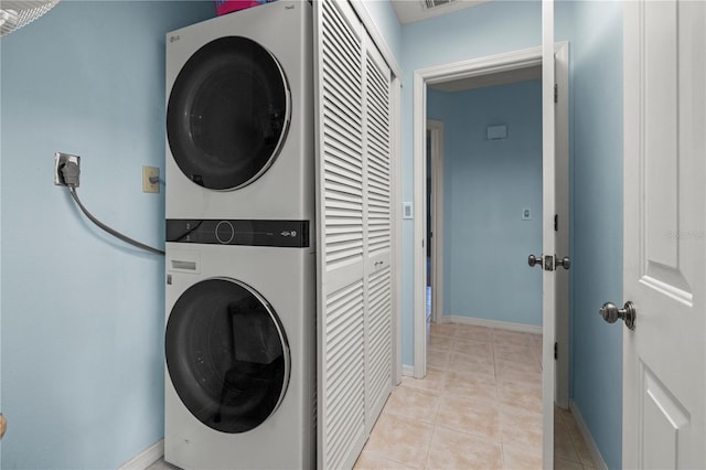 laundry area featuring light tile patterned floors, baseboards, stacked washer and dryer, and laundry area