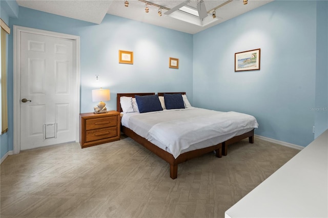 bedroom featuring baseboards, light carpet, a skylight, and track lighting