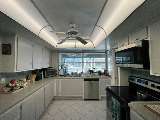 kitchen featuring a ceiling fan, a sink, stainless steel appliances, light tile patterned floors, and a raised ceiling