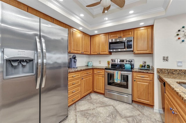 kitchen with a tray ceiling, ornamental molding, light stone counters, recessed lighting, and stainless steel appliances