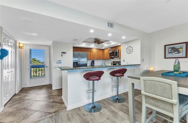 kitchen featuring stainless steel microwave, visible vents, refrigerator with ice dispenser, brown cabinetry, and a sink