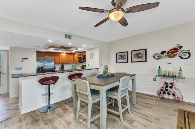 dining room with visible vents, a ceiling fan, a tray ceiling, light wood finished floors, and baseboards