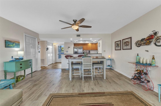 dining area featuring light wood-style flooring, a ceiling fan, visible vents, and baseboards