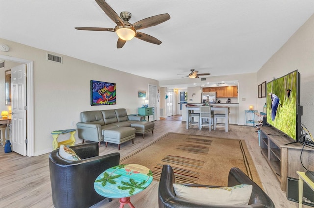 living room featuring visible vents, baseboards, ceiling fan, and light wood finished floors