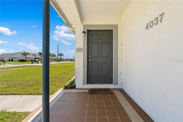 view of exterior entry with stucco siding and a lawn