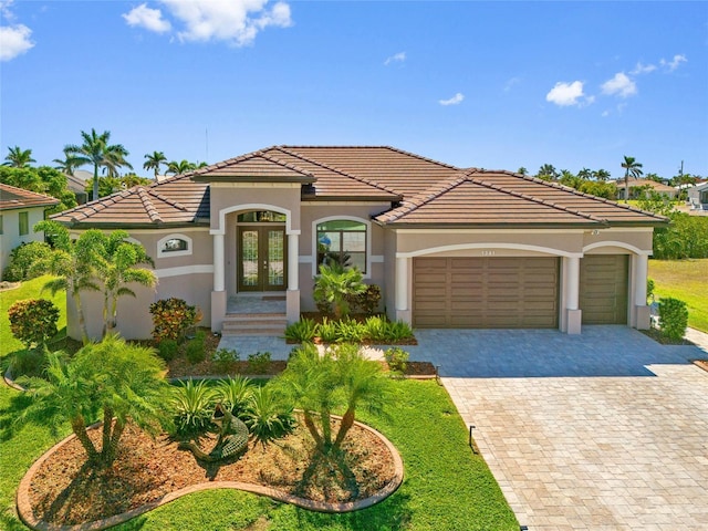 mediterranean / spanish house featuring french doors, a tile roof, stucco siding, and an attached garage