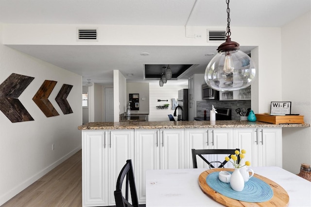 kitchen with stainless steel microwave, light wood-style flooring, a peninsula, and visible vents