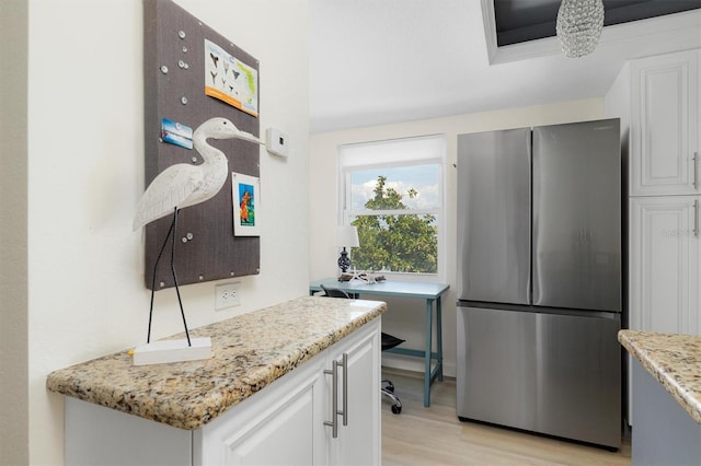 kitchen with light stone counters, light wood-style flooring, white cabinetry, and freestanding refrigerator