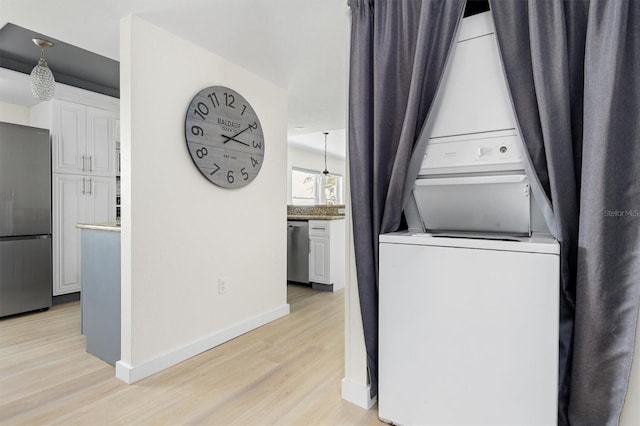 washroom with baseboards, light wood-style floors, stacked washer and clothes dryer, and laundry area