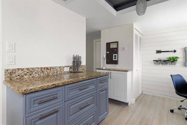 kitchen with stone counters, light wood-style floors, wood walls, and white cabinets