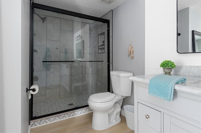 full bathroom with vanity, wood finished floors, a shower stall, a textured ceiling, and toilet