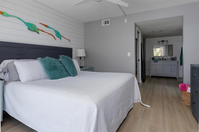 bedroom with visible vents, connected bathroom, ceiling fan, light wood-style floors, and a textured ceiling