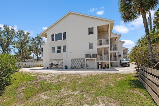 rear view of house featuring stucco siding, a balcony, and fence