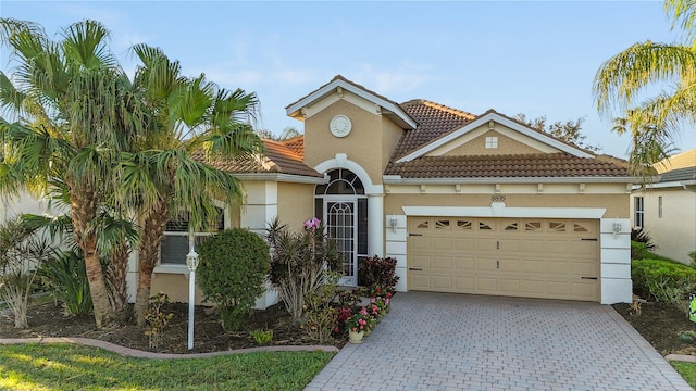 mediterranean / spanish-style home with stucco siding, a tiled roof, an attached garage, and decorative driveway