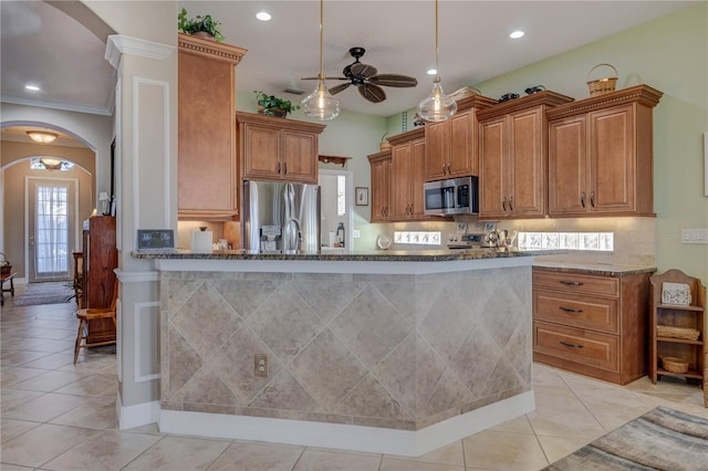 kitchen featuring dark stone counters, light tile patterned floors, brown cabinets, appliances with stainless steel finishes, and arched walkways