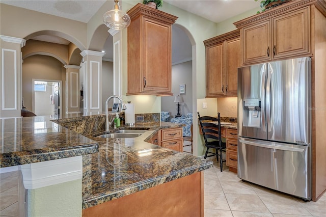 kitchen featuring stainless steel refrigerator with ice dispenser, a sink, a peninsula, brown cabinetry, and ornate columns