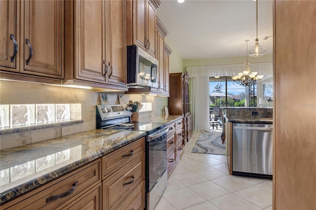 kitchen featuring brown cabinets, a notable chandelier, dark stone countertops, tasteful backsplash, and appliances with stainless steel finishes