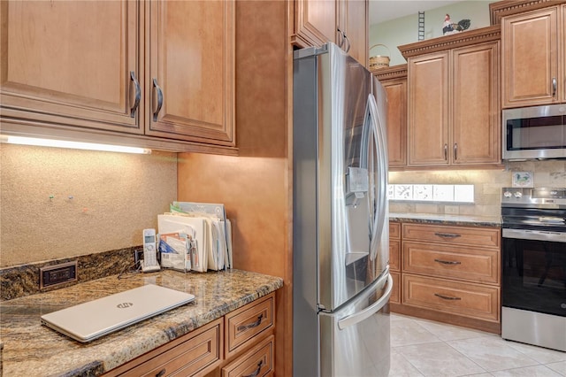 kitchen with backsplash, light tile patterned floors, brown cabinetry, stone countertops, and stainless steel appliances