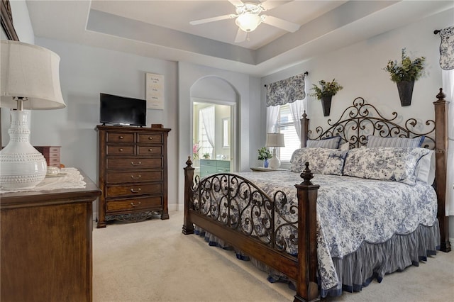 bedroom featuring ceiling fan, a tray ceiling, and light carpet