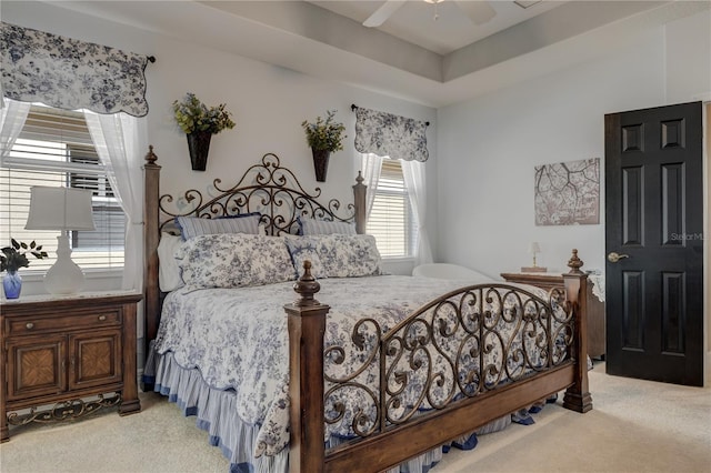 bedroom featuring light carpet, a raised ceiling, and a ceiling fan