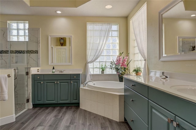 bathroom with two vanities, a stall shower, wood finished floors, recessed lighting, and a bath