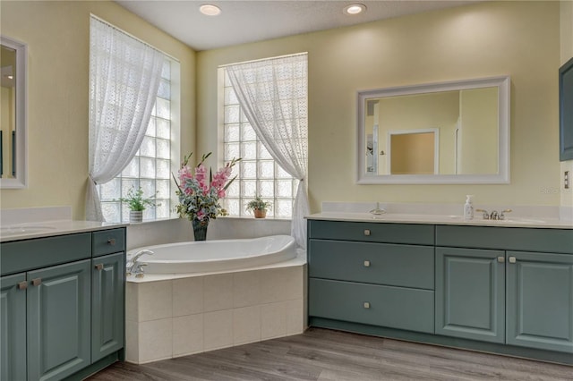 bathroom with a sink, a garden tub, two vanities, and wood finished floors