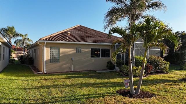 rear view of property with a lanai, stucco siding, a tiled roof, and a yard