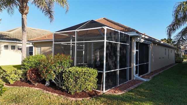 rear view of property featuring a tile roof, a lawn, a lanai, and stucco siding