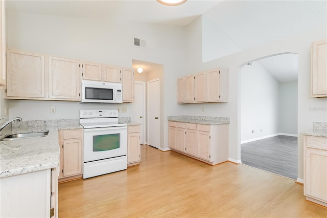 kitchen featuring visible vents, light brown cabinetry, arched walkways, white appliances, and a sink