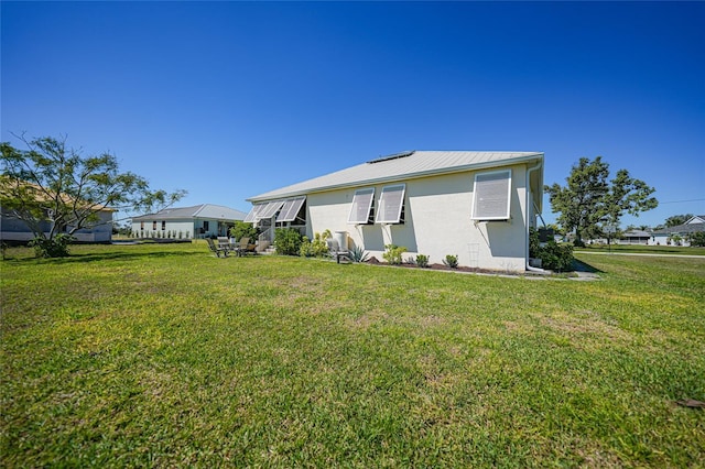 rear view of property with stucco siding, a lawn, and metal roof