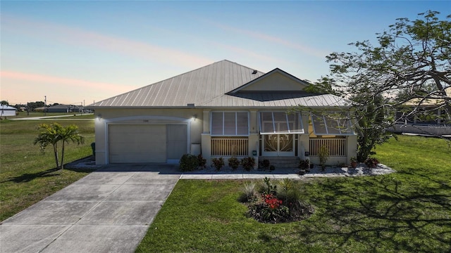 view of front of home with driveway, stucco siding, a front lawn, a garage, and metal roof